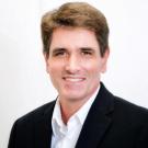 Michael smiles at the camera in a suit in front of a white background.